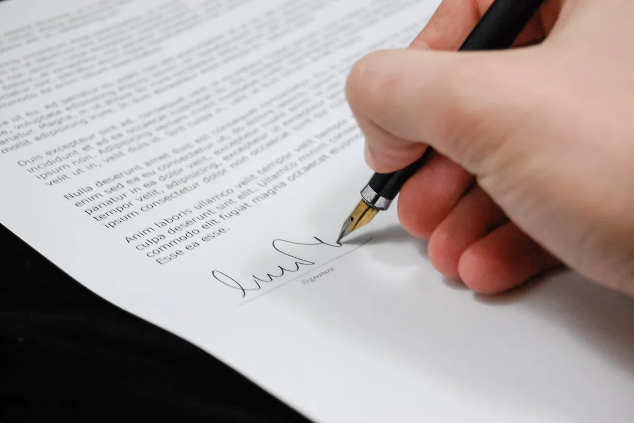 A person signing a contract with a pen on a wooden table, focused on the document in front of them.