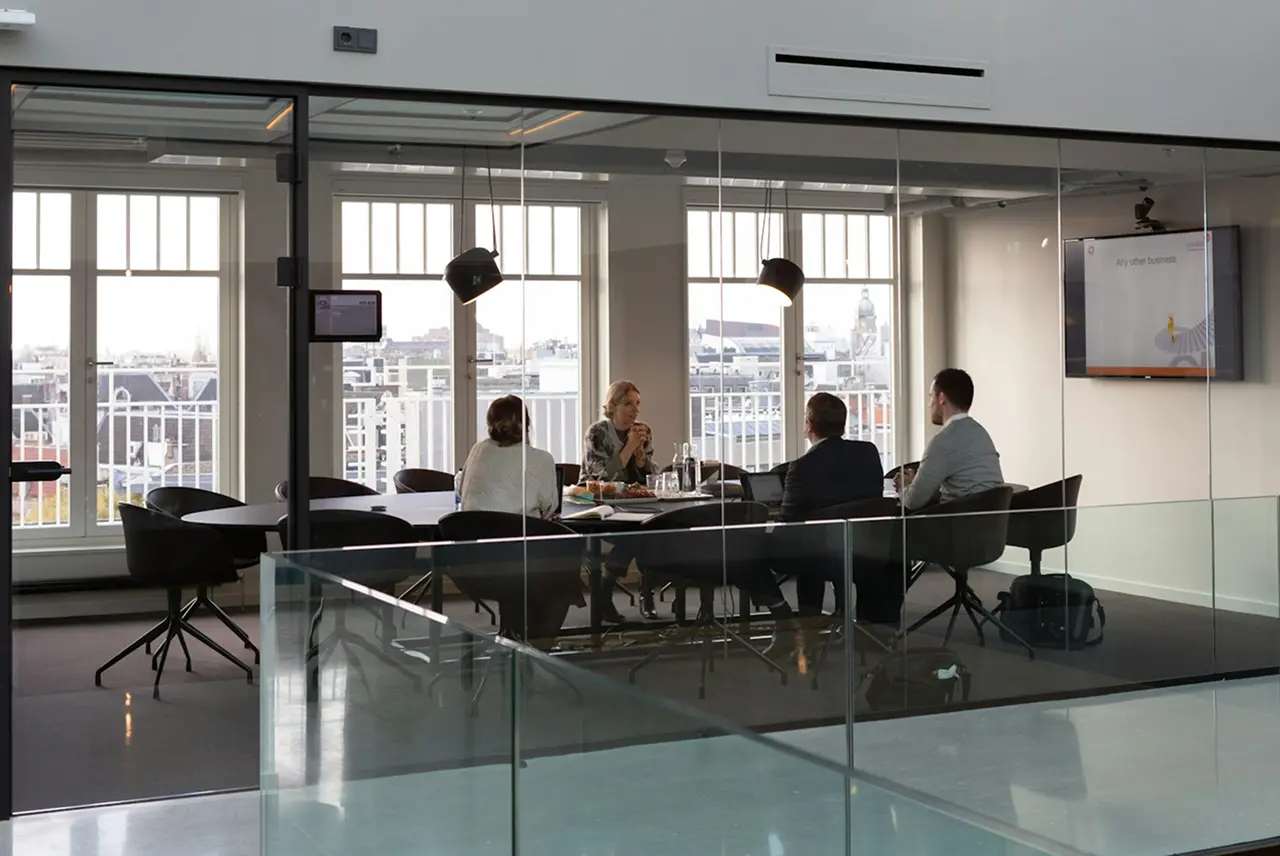 A group of diverse individuals seated around a table in a conference room engaged in discussion.