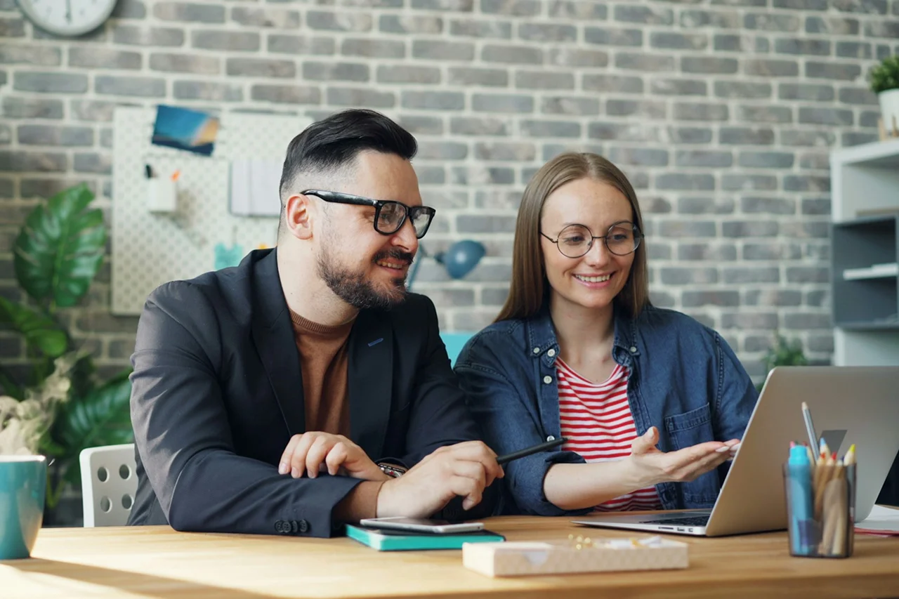 A man and woman sit at a table, working together on a laptop.